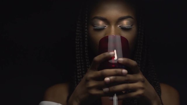 Big close-up of sexy attractive african american female model drinking a glass of red wine on black background in slow-motion