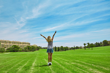 Happy beautiful woman in golf course. Wide green field and blue sky. Outstretched arms fresh morning air summer.
