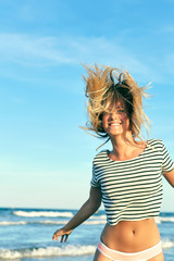 Beautiful woman in swimsuit jumping near the sea. Blonde girl in bikini having fun on vacation. Young woman shakes her hair on a background of the blue ocean.