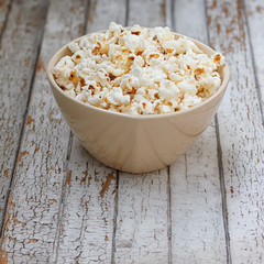 Fresh popcorn in bowl on white wooden table