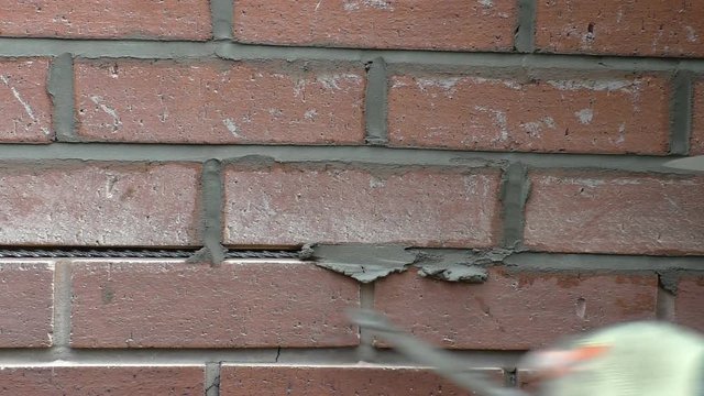 Close up of bricklayer working on brick wall crack repair.Long helibar is inserted into the gap after raking out old mortar and fresh mix tucked in using tuck pointing trowel.  