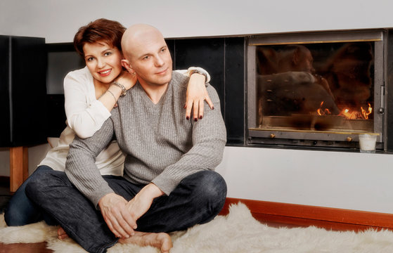 Beautiful couple sitting on fur carpet near the fireplace