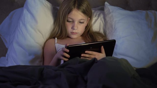 Young child at night with tablet in bed on the internet.