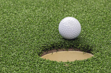 Golf  ball on lip of cup,close up view.