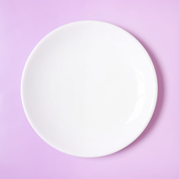 A Plain White Dinner Plate On A Pink Background