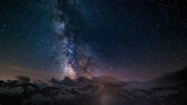 The apparent rotation of an outstandingly bright Milky Way and the starry sky beyond snowcapped mountain ridge, captured at high altitude in summertime on the Italian Alps. Time Lapse 4k video.