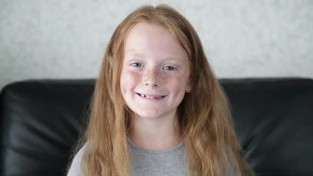 Little ginger girl is looking into the camera and smiling