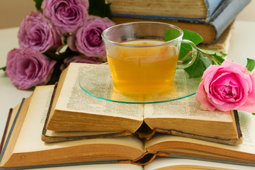 Cup of tea in glass cup with open old booksand roses
