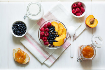 Healthy breakfast: muesli with honey, milk and fresh berries in a bowl on white wooden background