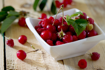 Ripe sweet cherries and raspberries in a bowl on a wooden table,