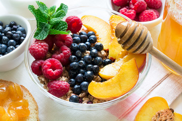 Healthy breakfast: muesli with honey, milk and fresh berries in a bowl on white wooden background