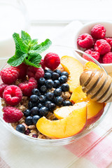 Healthy breakfast: muesli with honey, milk and fresh berries in a bowl on white wooden background