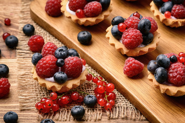 Tartlets with cream, blueberries, raspberries and red currants on brown wooden background.