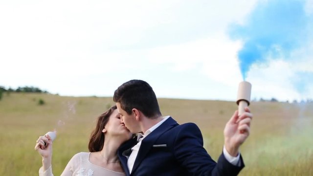 The bride, the groom and his friend posing in a field with smoke bombs.