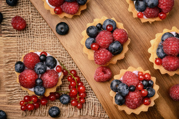 Tartlets with cream, blueberries, raspberries and red currants on brown wooden background. Top view.