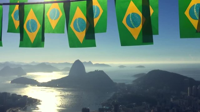 Brazilian flag bunting flying above skyline scenic overlook of Rio de Janeiro city with Sugarloaf Mountain Botafogo and Guanabara Bay in front of the rising sun