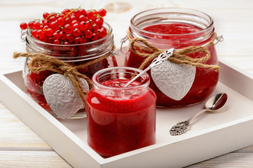 Red currants jam in glass jars on white wooden tray.