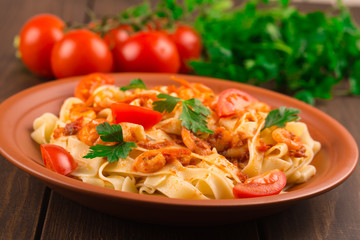 Fettuccine pasta with shrimp tomatoes and herbs. wooden background