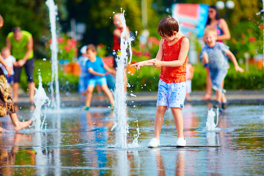 excited boy having fun between water splashes, in fountain. Summ