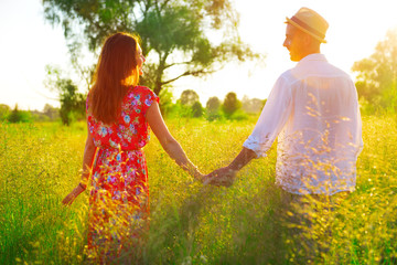 Couple holding hands and walking together on summer meadow field