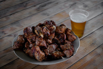Plate with roasted meat pieces and glass of beer on wooden table