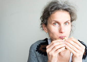 Middle aged woman with grey hair with mouthful of healthy salad sandwich