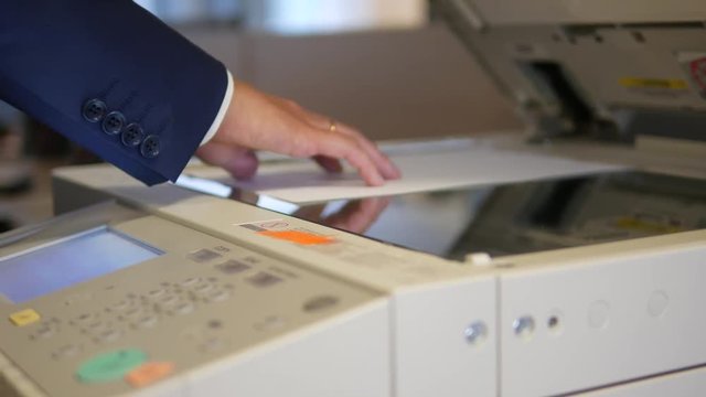 Man opening the lid of an office copier and putting a document for making a copy. Dolly shot