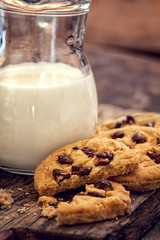 Chocolate chip cookies with milk in bottles on wooden background