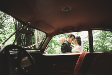 Happy newlywed couple, man and wife kissing near stylish retro car