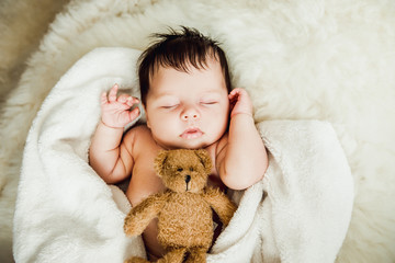 Newborn baby girl sleeps wrapped in white blanket.