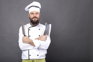 Studio shot of a happy bearded young chef holding sharp knives