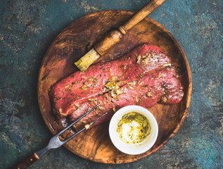 Raw meat marinating on wooden plate with rub brush , top view