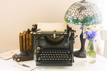 black vintage typewriter with books on wooden table with art nuveau lamp