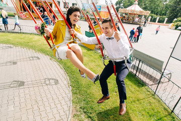 Emotional newlyweds laughing while riding on high carousel in amusement park. Expressive wedding...