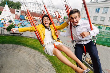 Emotional newlyweds screaming while riding on high carousel in amusement park. Expressive wedding...