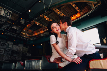 Closeup. The groom kisses his bride in vintage loft designed interior. She smiles and dreamily looks up. Wedding couple of stylish hipsters. Emotional sight