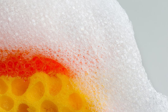 Cleaning sponge with soap foam on top. Macro view bubble suds, gray background. Cleaning supplies concept. soft focus