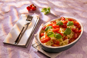Italian Farfalle pasta with tomatoes and basil over a colored ba