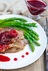Pork cutlets with raspberry sauce and asparagus on white plate