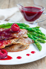 Pork cutlets with raspberry sauce and asparagus on white plate