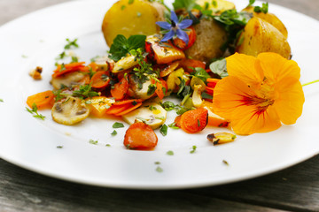 Veganes Essen - Gemüsepfanne mit essbaren Blüten, Kapuziner Kresse, Borretsch, Gartenkräuter  an der Gemüsepfanne