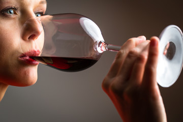 Elegant young woman in a red dress, having a glass of red wine