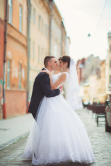 Naklejka premium Wedding photo shooting. Bride and bridegroom walking in the city. Married couple embracing and looking at each other. Holding bouquet. Outdoor, full body