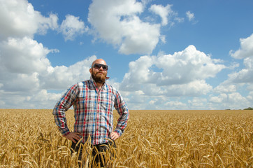 Naklejka na ściany i meble Happy smiling successful caucasian thirty years old farmer standing proud in front of his wheat fields