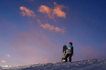 Naklejka na ściany i meble Girl snowboarder stands on a hillside against dark sunset sky