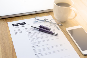 Businessman or job seeker review his resume on his desk before send to finding a new job with pen, computer laptop, glasses, a cup of coffee and smart phone.
