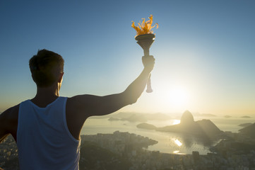 Torchbearer athlete holding sport torch standing in silhouette against the sunrise skyline of Rio de Janeiro, Brazil with Sugarloaf Mountain