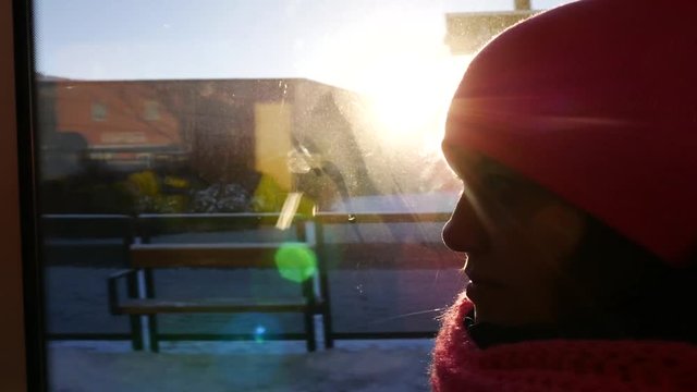 Pretty girl in pink cap riding public bus. Close up of face at the window with sun rays and highlights 