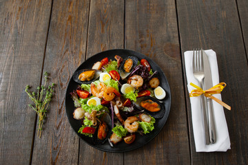 Portion of grilled seafood salad with cutlery on wood. Served with knife and fork and rosemary on white napkin salad wirh grilled seafood on wooden table