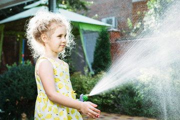 Little girl watering the grass in the garden